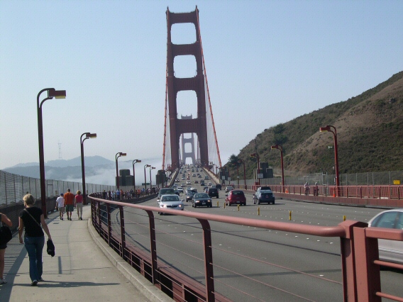 Bridge towers align as people and cars make the crossing